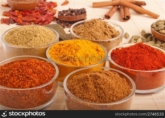 gorgeous setting with cooking spices and herbs (bay leaves, cumin, coriander, chili powder, cloves, cardamom pods, cinnamon sticks, paprika, piri piri, salt, turmeric) on a wooden mat (shallow DOF)