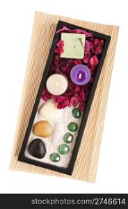 gorgeous spa setting with candles, stones, sand, rake, incense and dry petal roses on a black tray and wooden mat (isolated on white background)
