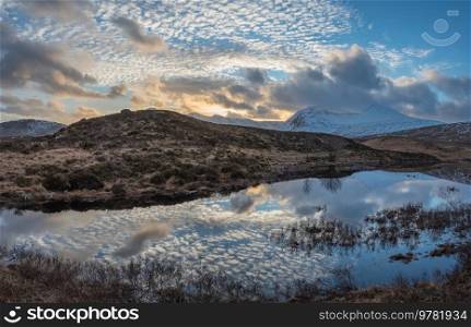 Gorgeous Winter sunset landscape image across Loch Ba in Scottish Highlands towards snow covered mountain range in distance