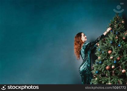 Gorgeous woman in a beautiful dress decorating Christmas tree. Copy space for your text and design. Luxury green, blue, golden colors. Home and family warmth. Banner for holiday theme