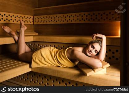 Gorgeous woman relaxing in sauna. Spa beauty treatment and lifestyle relaxation concept: Woman in yellow towel is relaxing in wooden Finish sauna room