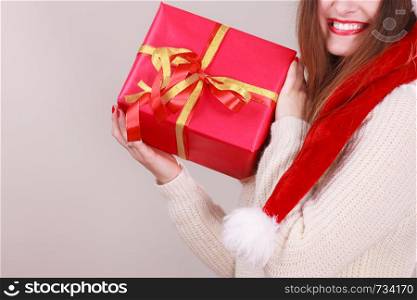 Gorgeous woman wearing santa claus hat holding red big gift box with ribbon. Xmas, happiness, winter and people concept.. Woman holding gift box. Christmas time