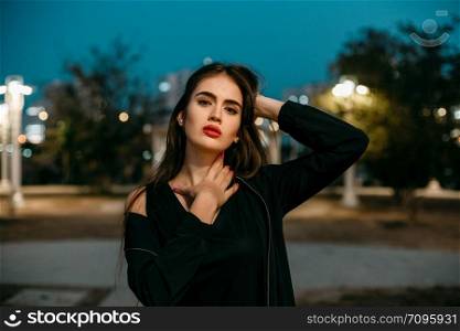 Gorgeous young model woman looking at camera posing in the city wearing black evening dress.