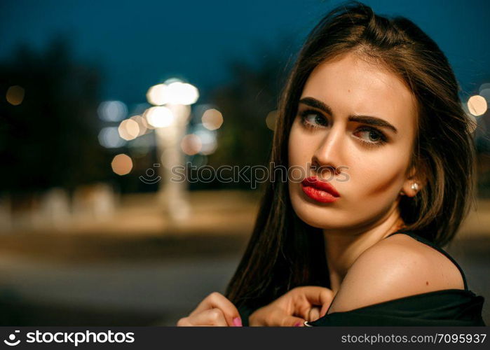 Gorgeous young model woman looking at camera posing in the city wearing black evening dress.