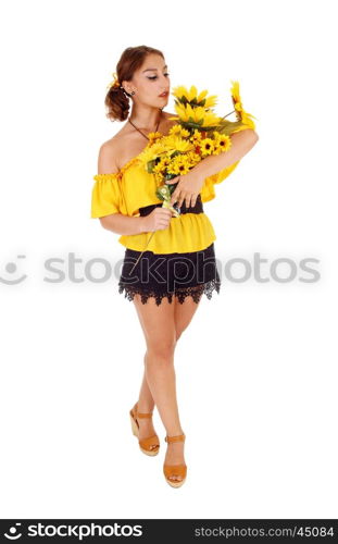 Gorgeous young woman in a yellow blouse holding a bunch of sunflowers, looking at them, standing isolated for white background.