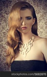 gorgeous young woman with long wavy hair-style, creative necklace, stylish make-up and sexy dark dress posing in fashion shoot with charming expression