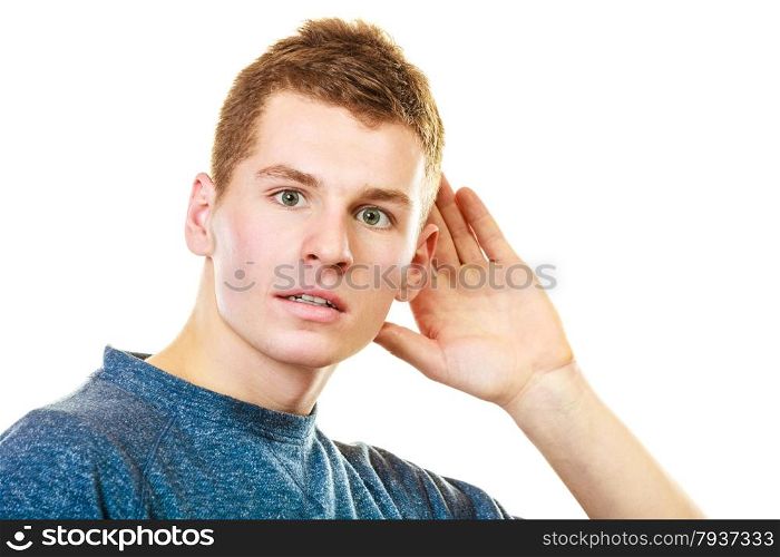 Gossip. Young man holding hand to ear listening isolated on white background