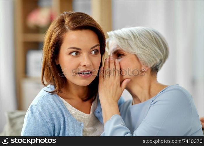 gossiping and family concept - senior mother whispering secret to adult daughter at home. senior mother whispering to adult daughter at home