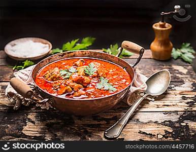 Goulash or stew in copper pan with spoon on rustic kitchen table over dark wooden background