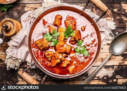 Goulash or stew in vintage pot with tomtoes sauce on rustic wooden background, top view
