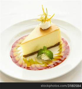 Gourmet slice of cheesecake garnished with zest and sauce and mint sprig.