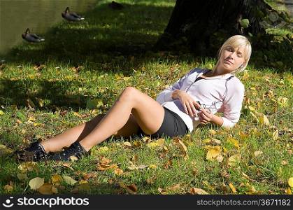 graceful blond girl enjoying the sun and music laying on the grass