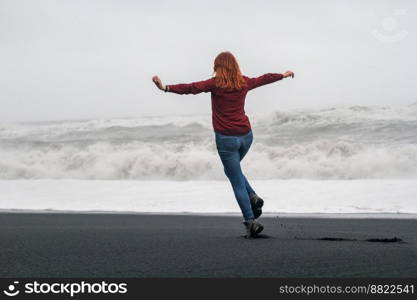 Graceful woman having fun on black beach scenic photography. Picture of person with stormy sea on background. High quality wallpaper. Photo concept for ads, travel blog, magazine, article. Graceful woman having fun on black beach scenic photography