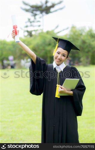 Graduate woman students wearing graduation hat and gown and holding tablet