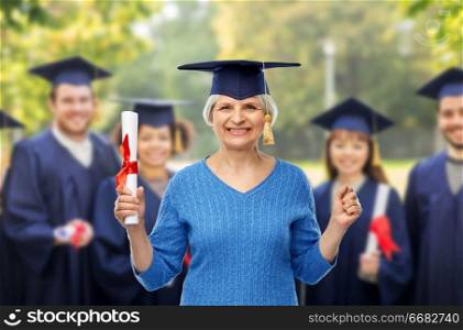 graduation, education and old people concept - happy senior graduate student woman in mortar board with diploma over group of students background. happy senior graduate student woman with diploma