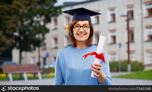 graduation, education and old people concept - happy senior graduate student woman in mortar board with diploma laughing over university campus background. happy senior graduate student woman with diploma