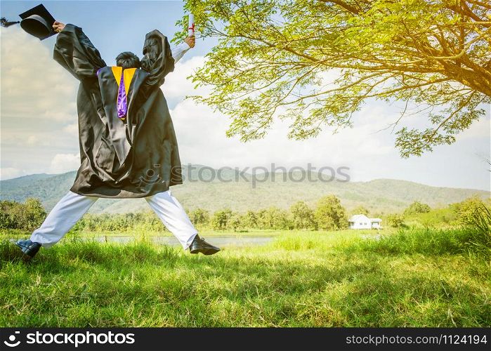 Graduation: Student standing up and jumping holding Graduation certificate with Diploma With background in the nature.