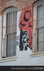 Graffiti painted between two windows on brick wall