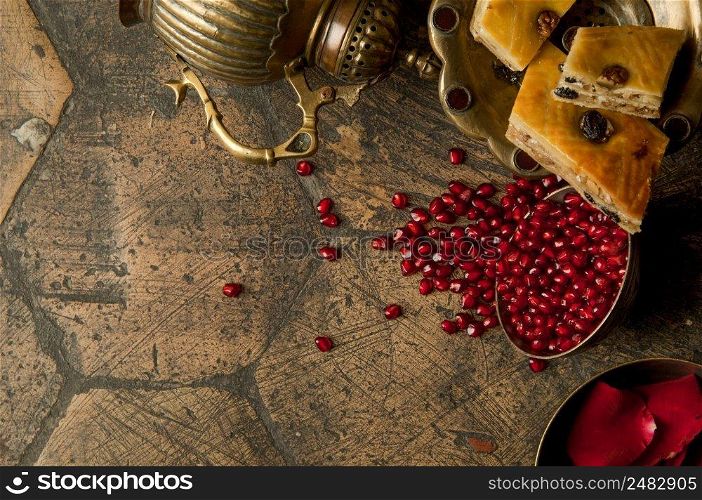 grains and seeds of pomegranate with a copper jug on an old decorative paving sto≠. an antique copper jug with a pomegranate and cake on an old ti≤. grains of pomegranate on old paving sto≠s