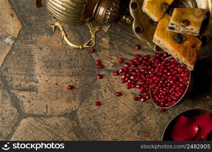 grains and seeds of pomegranate with a copper jug on an old decorative paving sto≠. an antique copper jug with a pomegranate and cake on an old ti≤. grains of pomegranate on old paving sto≠s