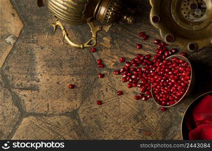 grains and seeds of pomegranate with a copper jug on an old decorative paving stone. antique copper jug with a pomegranate on an old tile. grains of pomegranate on old paving stones