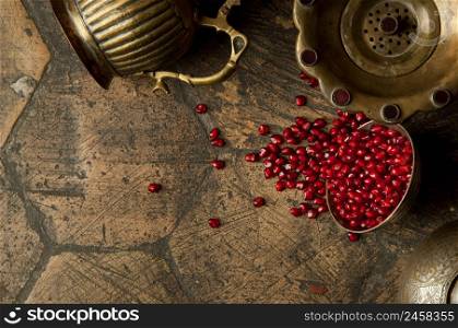 grains and seeds of pomegranate with a copper jug on an old decorative paving stone. antique copper jug with a pomegranate on an old tile. grains of pomegranate on old paving stones