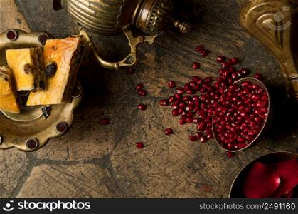 grains and seeds of pomegranate with a copper jug on an old decorative paving stone. an antique copper jug with a pomegranate and cake on an old tile. grains of pomegranate on old paving stones