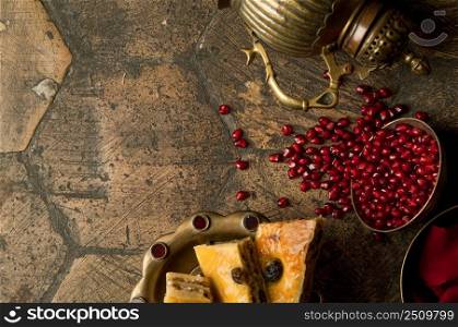 grains and seeds of pomegranate with a copper jug on an old decorative paving stone. an antique copper jug with a pomegranate and cake on an old tile. grains of pomegranate on old paving stones