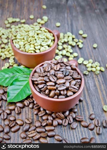 Grains of green and black coffee in brown clay cups and on a table with leaves on a background of a dark wooden board