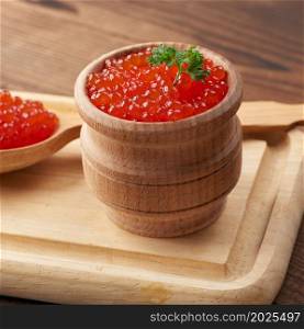 grainy red caviar in a wooden bowl on a brown table