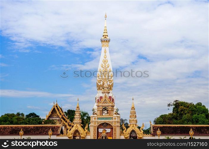 Grand ancient pagoda of Wat Phra That Phanom against sky, most sacred temple of Nakhon Phanom - Thailand. Name of Wat Phra That Phanom written in Thai at top of the gate