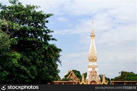 Grand ancient pagoda of Wat Phra That Phanom against sky, most sacred temple of Nakhon Phanom - Thailand. Name of Wat Phra That Phanom written in Thai at top of the gate
