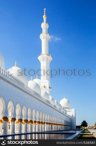 Grand white marble Minaret Azan tower of Sheikh Zayed Mosque against blue sky and pool garden terrace Abu Dhabi. UAE