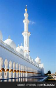Grand white marble Minaret Azan tower of Sheikh Zayed Mosque against blue sky and pool garden terrace Abu Dhabi. UAE