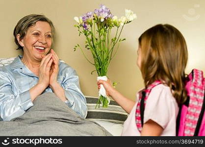 Grandchild giving bouquet of flowers to grandmother lying in bed