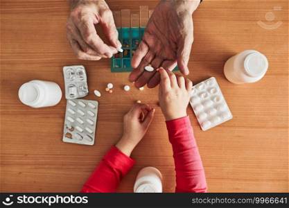 Grandchild helping grandfather to organize medication into pill dispenser. Senior man taking pills from box. Healthcare and old age concept with medicines. Medicaments on table
