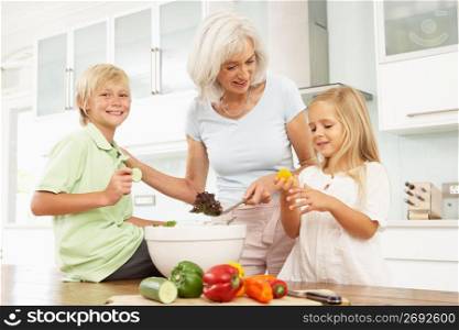 Grandchildren Helping Grandmother To Prepare Salad In Modern Kitchen