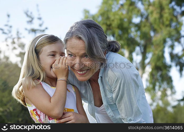 Granddaughter (5-6) whispering to grandmother&acute;s ear, outdoors