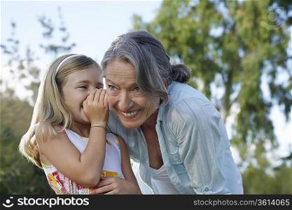 Granddaughter (5-6) whispering to grandmother&acute;s ear, outdoors