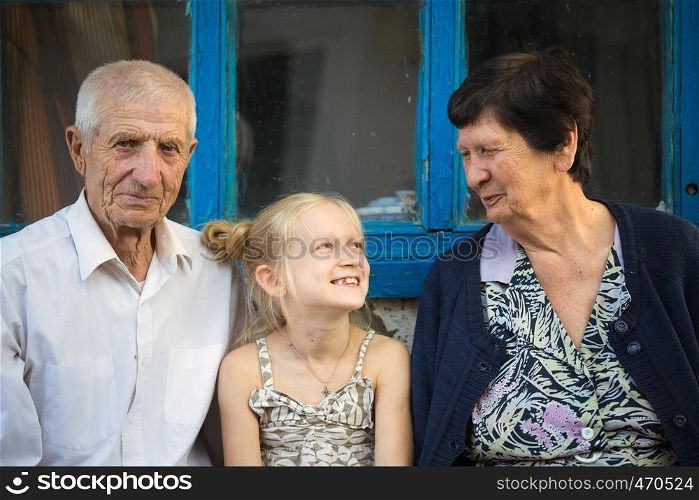 granddaughter embracing with grand parents sitting at the front of rural house