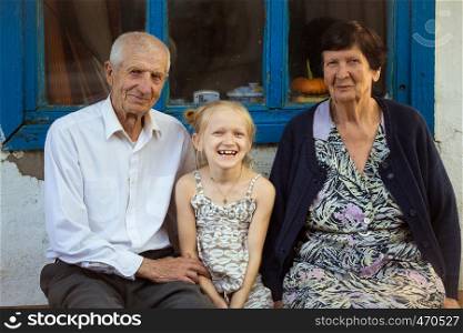 granddaughter embracing with grand parents sitting at the front of rural house