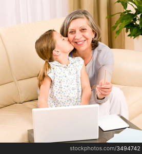 Granddaughter giving kiss to grandmother smiling together on sofa