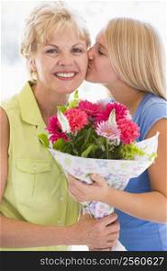 Granddaughter kissing grandmother on cheek holding flowers and smiling