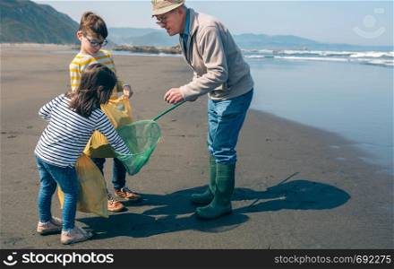 Grandfather and grandchildren taking garbage out of the sea with a fishing net. Volunteers taking garbage out of the sea