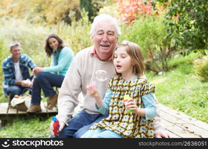 Grandfather And Granddaughter Blowing Bubbles On Family Picnic