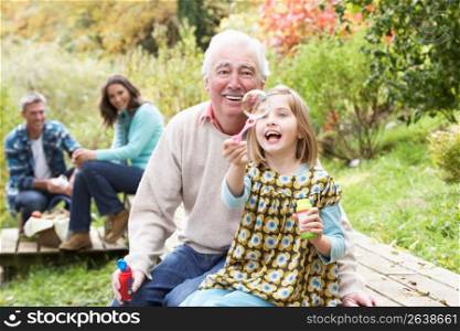 Grandfather And Granddaughter Blowing Bubbles On Family Picnic