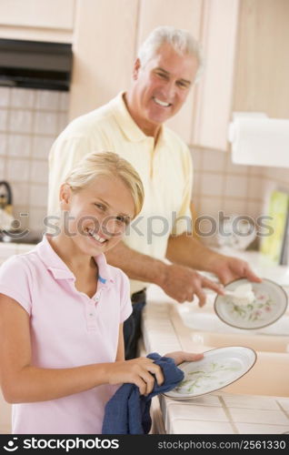 Grandfather And Granddaughter Cleaning Dishes Together