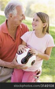 Grandfather and granddaughter outdoors with ball smiling