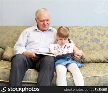 grandfather and granddaughter sitting on the sofa and reading book