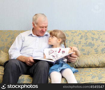 grandfather and granddaughter sitting on the sofa and reading book